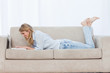 Side view shot of a smiling woman lying on a couch typing on her