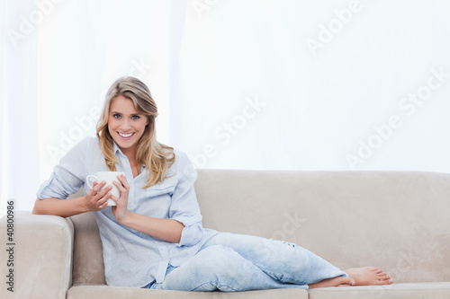 Foto: A woman holding a cup of coffee is sitting on a couch A woman holding a cup of coffee is sitting on a couch