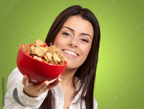 Photo: portrait of young woman offering cereals bowl over green backgro portrait of young woman offering cereals bowl over green backgro