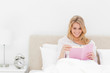 Woman in bed sitting upright, reading a book and smiling