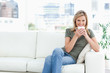 Foto: Woman smiling with a cup near her lips, sitting on the couch and Woman smiling with a cup near her lips, sitting on the couch and