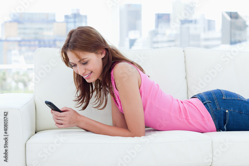 Photo: Young woman lying on a comfortable sofa while sending a text Young woman lying on a comfortable sofa while sending a text