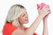 Fair-haired woman shaking a pink piggy bank