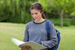 Young serious woman reading her notebook while standing in a par