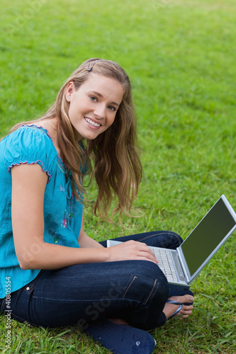 Photo: Young smiling girl looking at the camera while using her laptop Young smiling girl looking at the camera while using her laptop