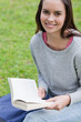 canvas print picture - Young smiling woman reading a book in a park while looking at th