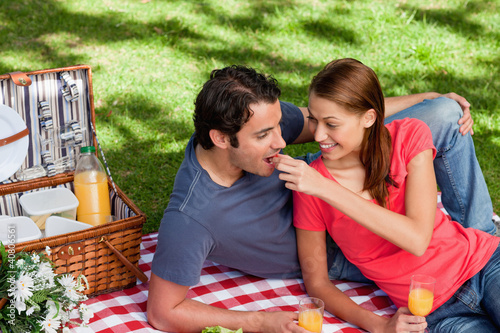Foto: Young woman feeding her friend as they as they lie on a blanket Young woman feeding her friend as they as they lie on a blanket