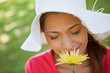 Woman wearing a white hat while smelling a flower with her eyes