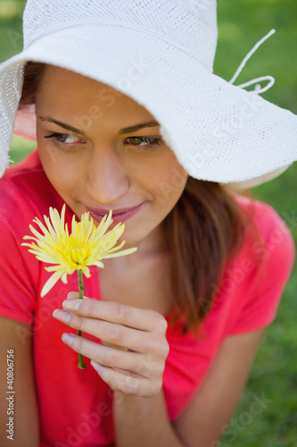 Photo: Woman wearing a white hat while smelling a flower while looking Woman wearing a white hat while smelling a flower while looking