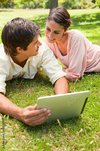 Photo: Two friends looking at each other while using a tablet together Two friends looking at each other while using a tablet together