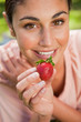 canvas print picture - Woman offering a strawberry while lying in grass
