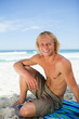 Foto: Smiling man sitting on his beach towel while looking at the came Smiling man sitting on his beach towel while looking at the came