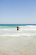 Rear view of a blonde man running in the water with his surfboar