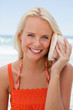 Young smiling woman holding a shell to hear the sound of the sea