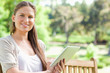 Smiling woman with a tablet on a park bench