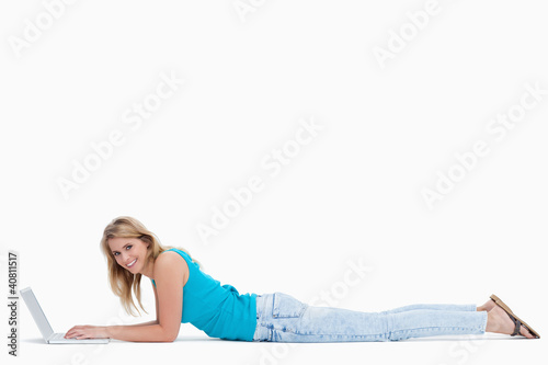 Photo: A woman smiling at the camera is lying on the ground typing on h A woman smiling at the camera is lying on the ground typing on h
