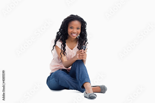 Photo: A smiling woman sitting on the floor is holding a mobile phone A smiling woman sitting on the floor is holding a mobile phone