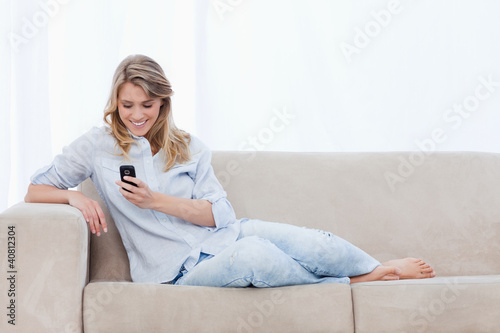 Foto: A woman sitting on a couch is holding a mobile phone A woman sitting on a couch is holding a mobile phone