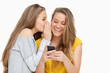 Young woman whispering to her friend who's texting on her phone