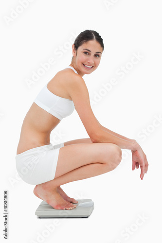 Photo: Slim young woman smiling while sitting on a scales Slim young woman smiling while sitting on a scales