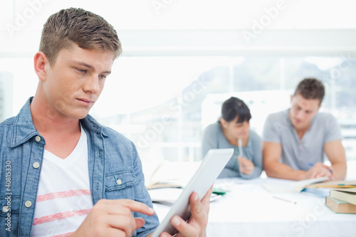 Photo: A man with a tablet pc works in front of his friends A man with a tablet pc works in front of his friends
