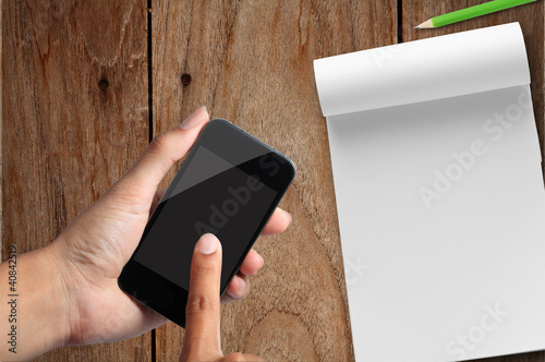 Photo: business hand with smart phone and note paper on wooden table business hand with smart phone and note paper on wooden table
