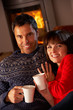 Middle Aged Couple Sitting On Sofa By Cosy Log Fire With Hot Dri