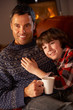 Father And Son Relaxing With Hot Drink Watching TV By Cosy Log F