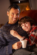 Father And Son Relaxing With Hot Drink Watching TV By Cosy Log F