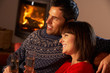 Middle Aged Couple Sitting Sofa By Cosy Log Fire With Glass Of C