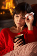 Sick Woman With Cold Resting On Sofa By Cosy Log Fire