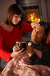 Wife Nursing Sick Husband With Cold Resting On Sofa By Cosy Log