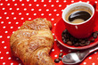 A red cup of coffee with croissant on red background