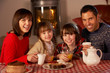 Portrait Of Family Enjoying Tea And Cake By Cosy Log Fire