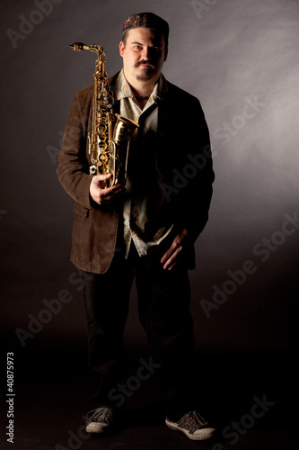 Photo: Jazzman standing with saxophone on dark background Jazzman standing with saxophone on dark background