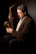 Jazz singer, siting down, saxophone in hands, looking away