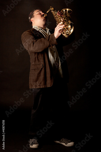 Photo: Jazzman standing playing saxophone on a dark background, low key Jazzman standing playing saxophone on a dark background, low key