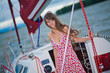 Beautiful girl in light dress standing on the deck of sailboat