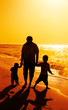 Father and two kids silhouettes on the beach at sunset