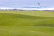 Golf course greens leading to the hole by the ocean