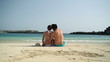 Couple sitting close together on the beach, rear view