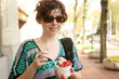 Foto: Young woman enjoying frozen yogurt in a cup in the city Young woman enjoying frozen yogurt in a cup in the city