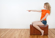 Young woman sitting on a suitcase and pointing direction Young woman sitting on a suitcase and pointing direction