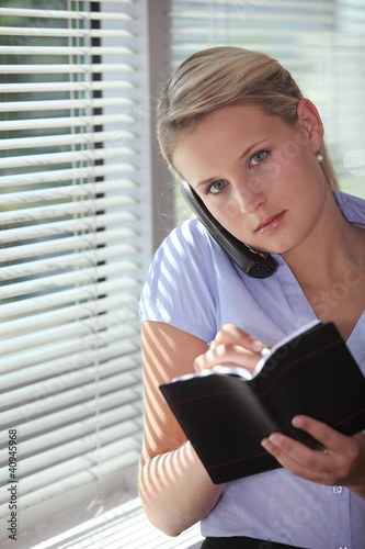 Foto: secretary talking on the phone and writing in her agenda secretary talking on the phone and writing in her agenda