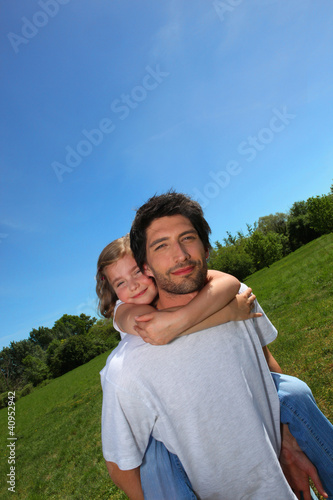 Foto: Man carrying little girl on his back in a meadow Man carrying little girl on his back in a meadow