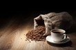 Coffee cup with burlap sack of roasted beans on rustic table Coffee cup with burlap sack of roasted beans on rustic table