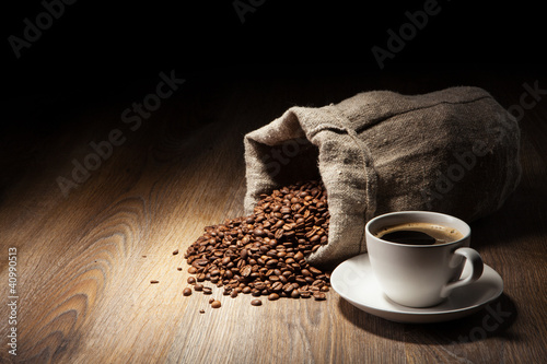 Photo: Coffee cup with burlap sack of roasted beans on rustic table Coffee cup with burlap sack of roasted beans on rustic table