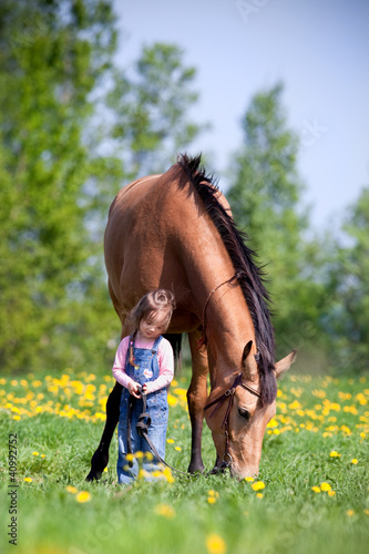 Photo: Child and big horse standing in the field at spring. Child and big horse standing in the field at spring.
