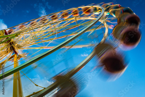 Photo: Blurry ferris wheel in motion on blue sky background Blurry ferris wheel in motion on blue sky background