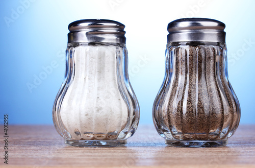 Photo: Salt and pepper mills on wooden table on blue background Salt and pepper mills on wooden table on blue background